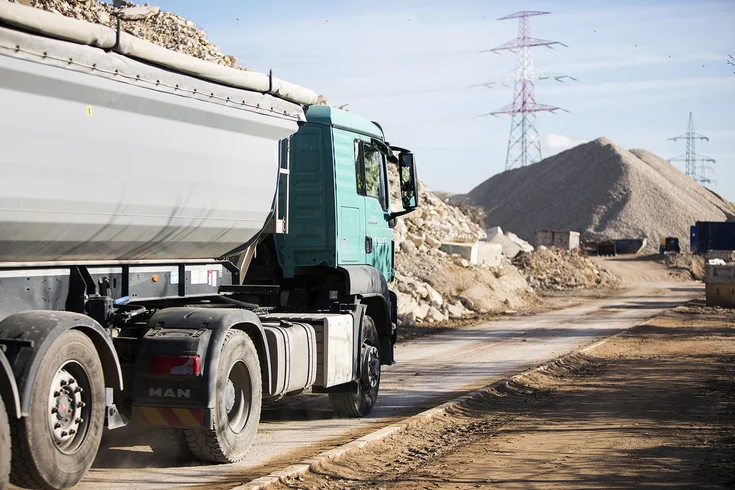 Foto: Lastwagen mit Mulde voller recycelter Baurestmassen unterwegs am Gelände des Recycling Center Himberg; im Hintergrund weitere Schuttberge und Strommasten.