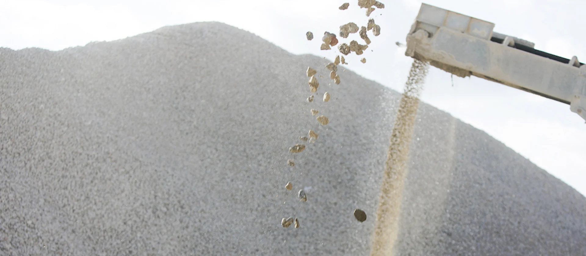 Foto: auf einen Haufen fallende, einzelne Stücke von Baurestmassen, rechts im Bild Schutt transportierendes Beförderungsband, weitere Haufen in der Aufschüttungsphase, im Hintergrund unscharf großer Schuttberg